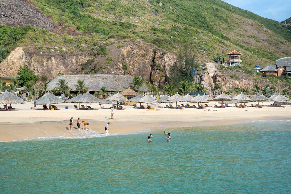 People relaxing on sandy beach with umbrellas and deckchairs washed by turquoise seawater and surrounded by tough grassy hills