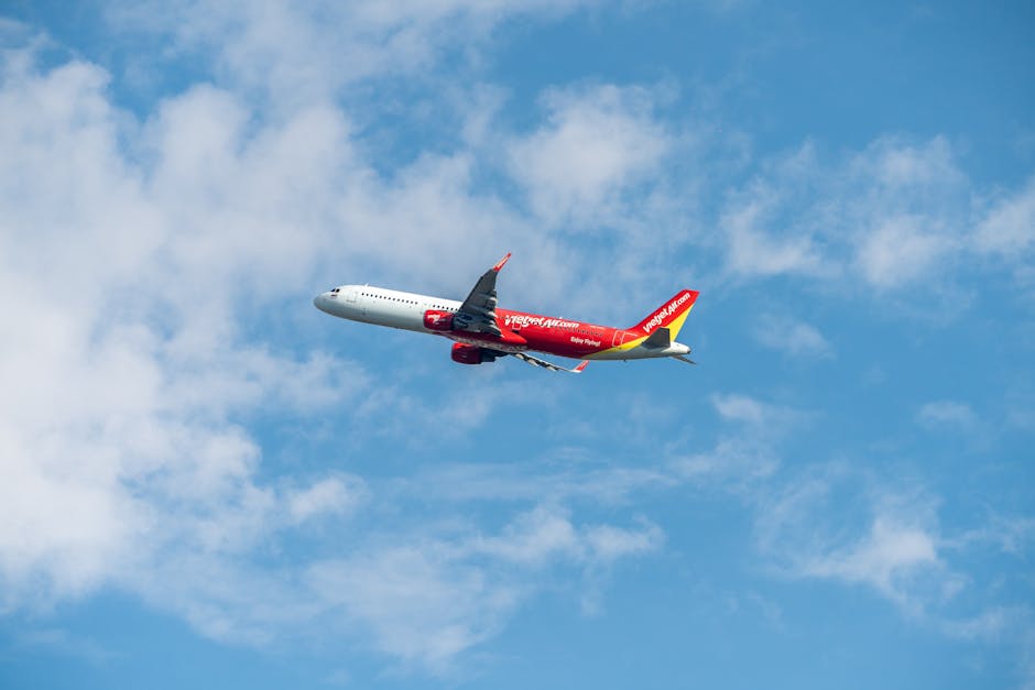 A red and white commercial airplane flying against a clear blue sky with fluffy clouds.